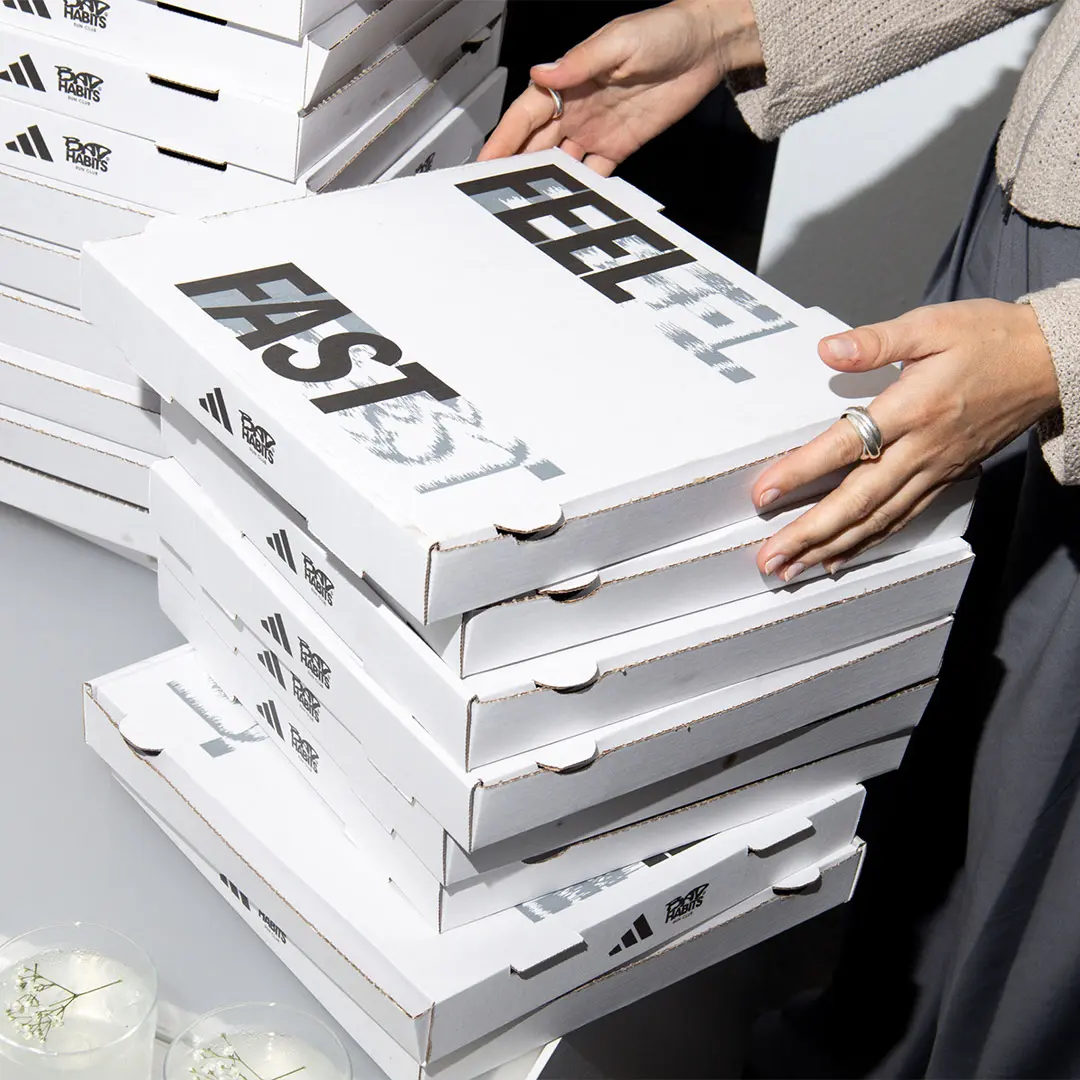 Person holding a stack of white pizza boxes with 'FEEL FAST' printed on the top box.