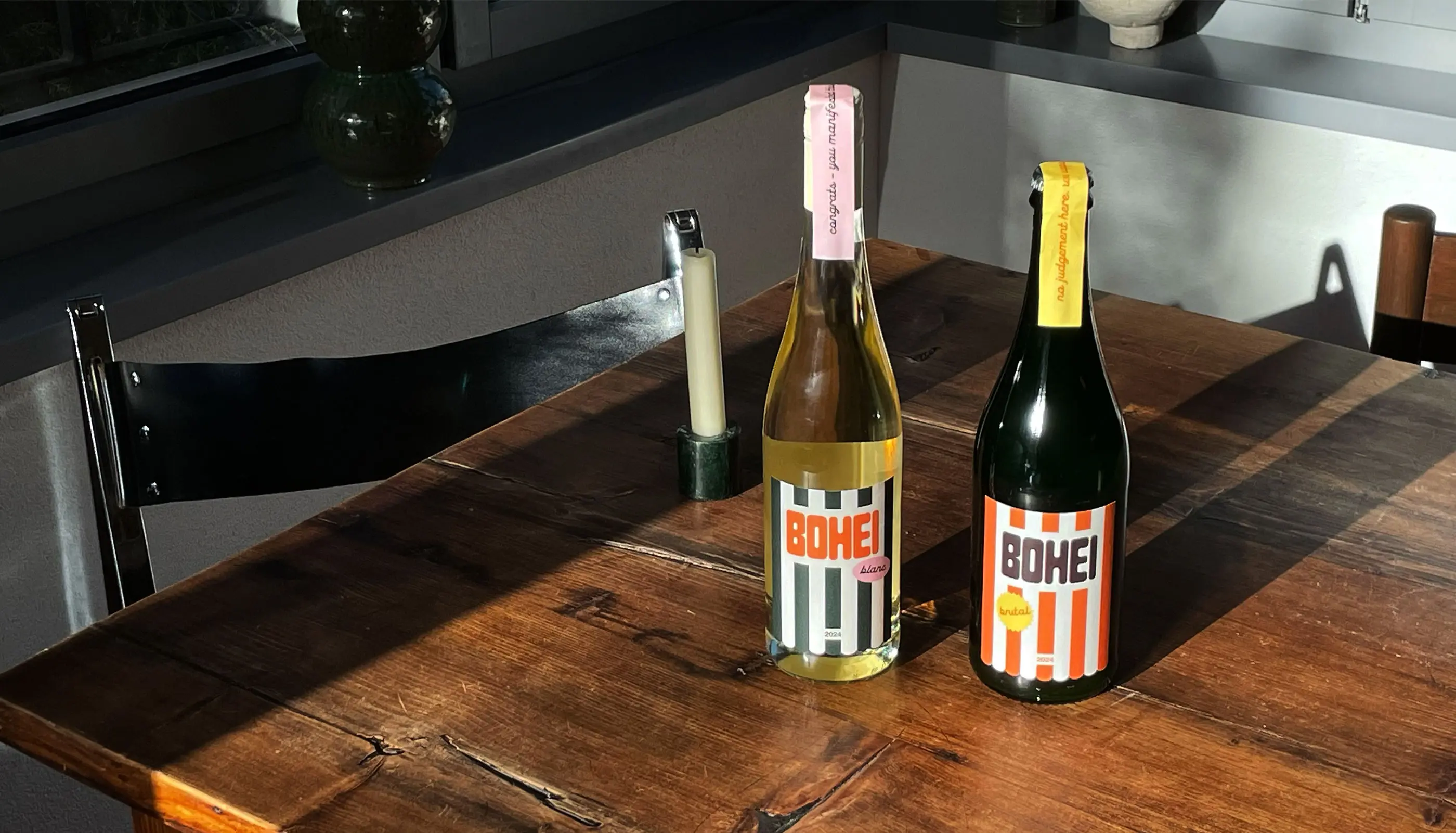 Two bottles of Bohei wine, one white and one red, placed on a wooden table with sunlight casting shadows.